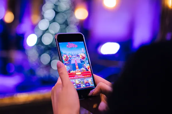 একজন তরুণী তার ফোনে আরাম করে গেম খেলছেন, আর চারপাশে ভাসছে ডায়নামিক ক্যাসিনো উপাদান—যা CD44 অ্যাপের মসৃণ মোবাইল অভিজ্ঞতাকে ফুটিয়ে তোলে।